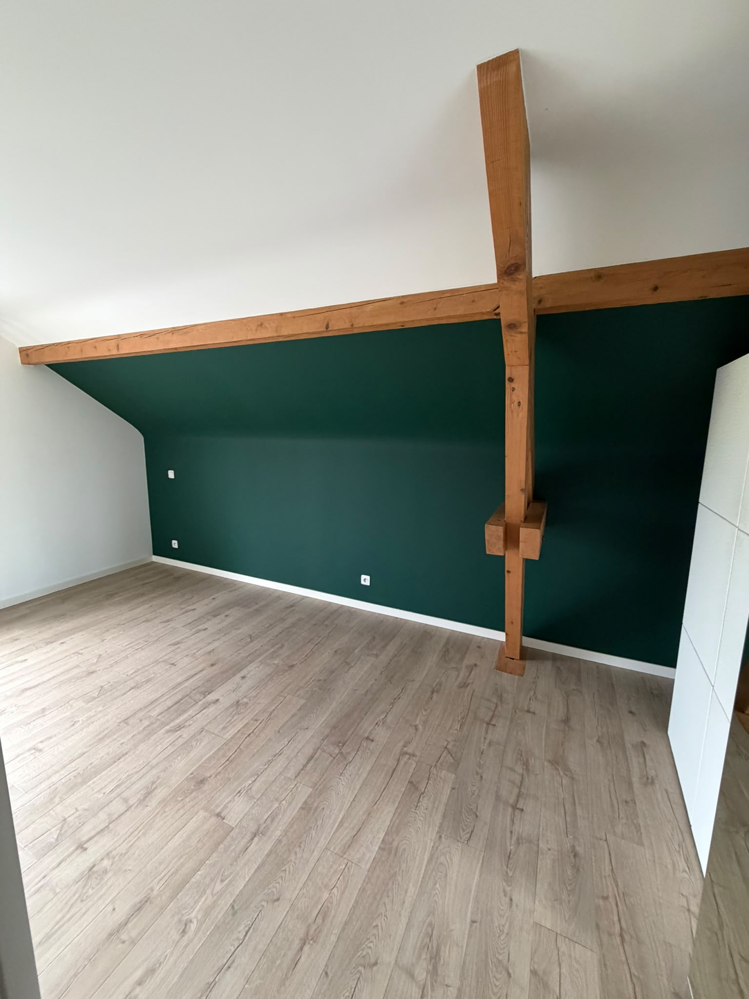 Combles aménagés avec un mur peint en vert sapin, poutres en bois apparentes et plafond blanc