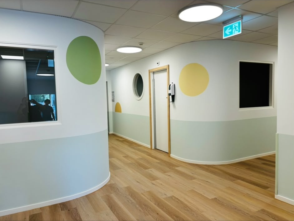 Couloir de crèche repeint : soubassement vert pâle, cercles vert et jaune peints au mur