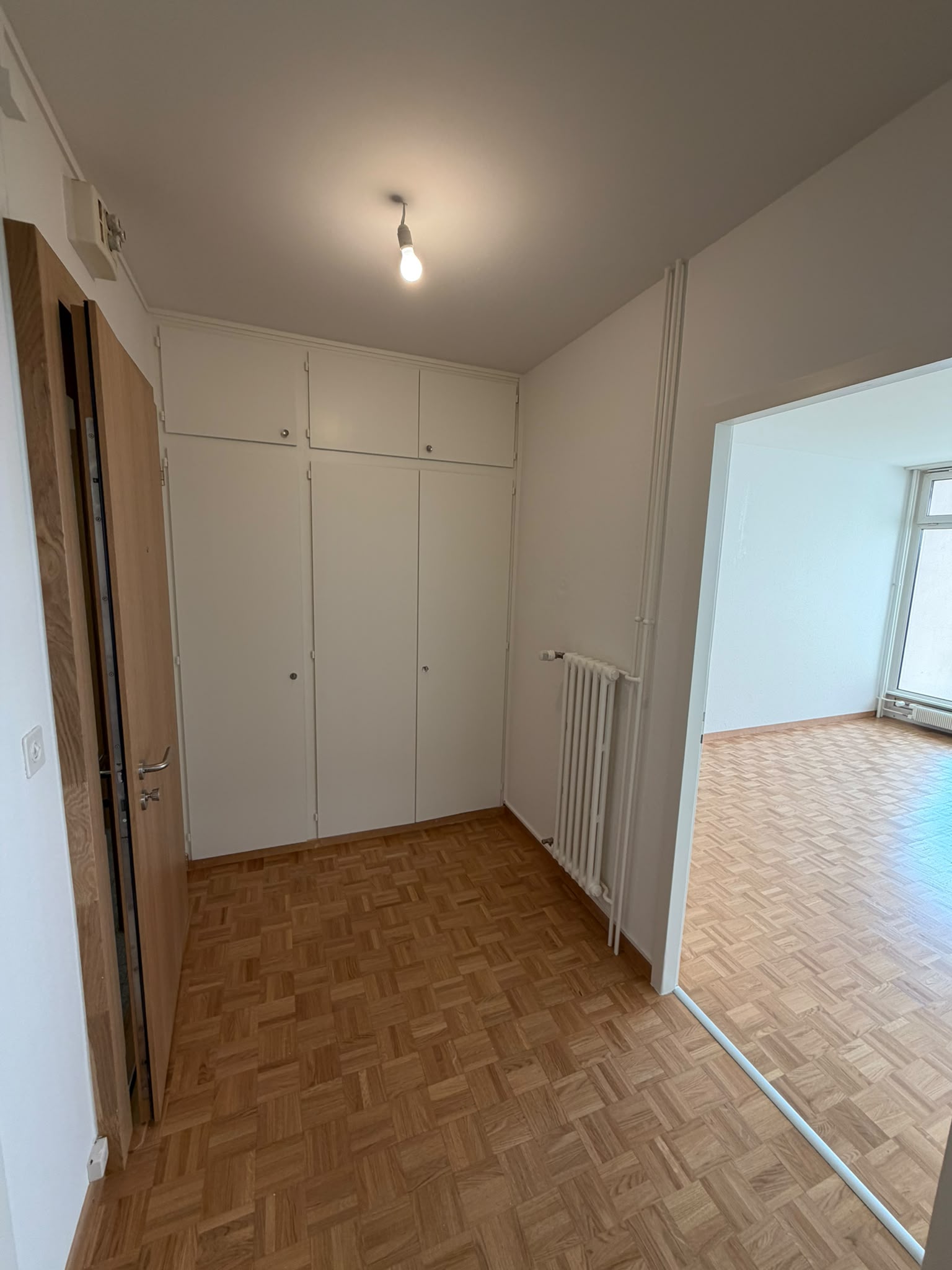 Entrée d’appartement repeinte en blanc avec armoires encastrées laquées et parquet mosaïque