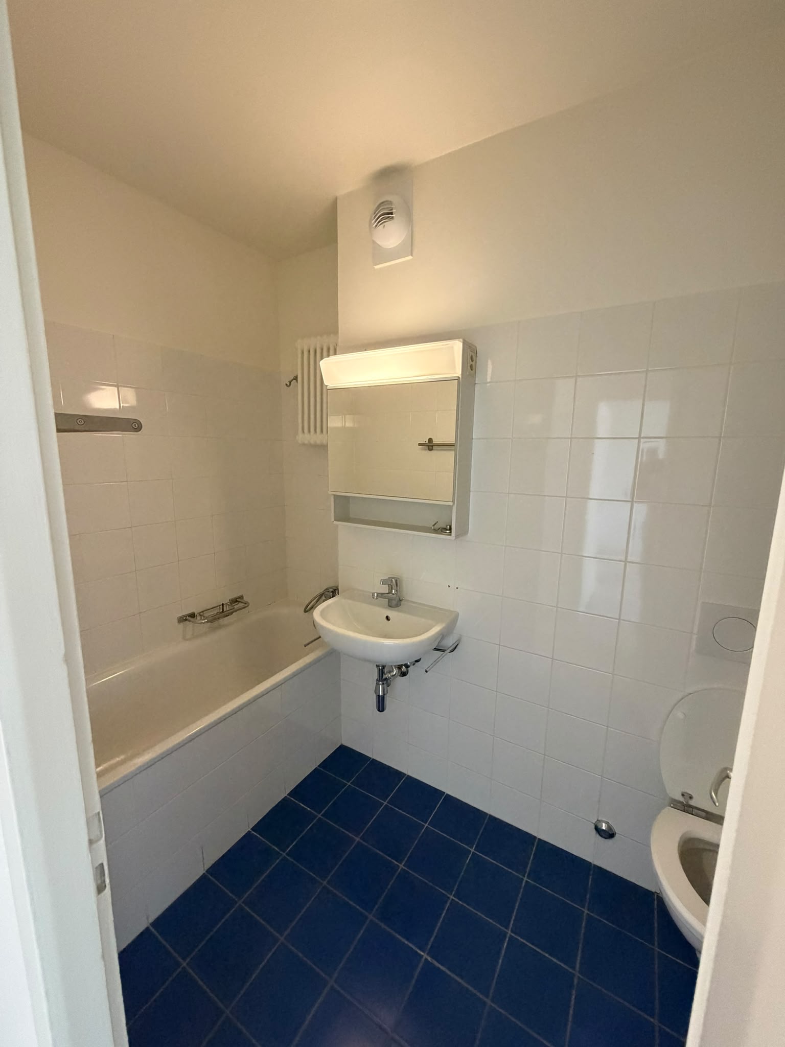 Salle de bains aux murs et plafond repeints en blanc au-dessus du carrelage, sol carrelé bleu