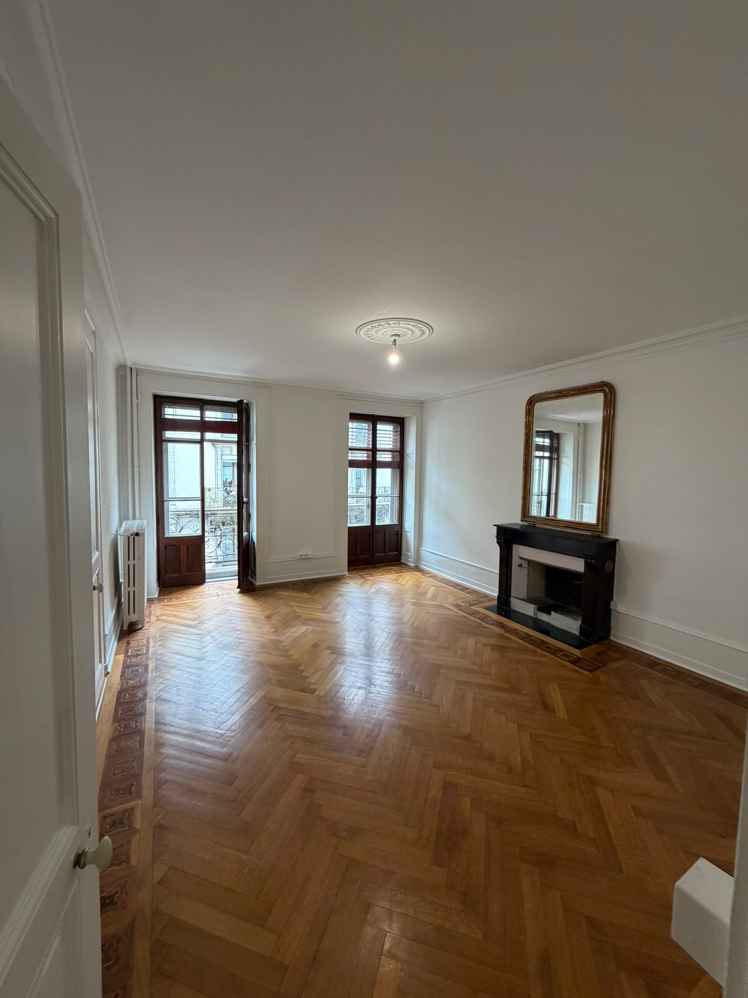 Salon d’appartement ancien repeint en blanc : cheminée en marbre noir, miroir doré, portes-fenêtres