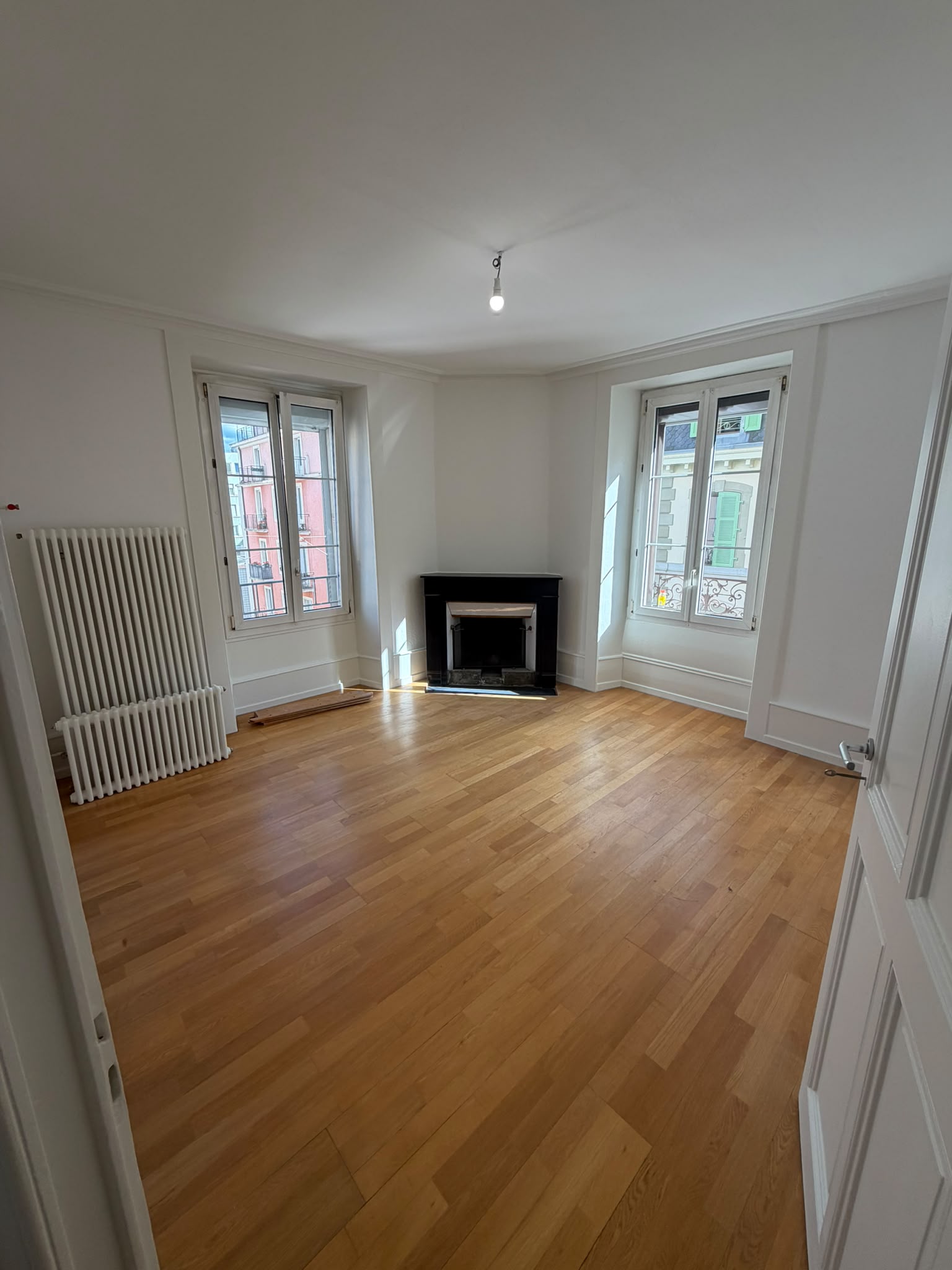 Séjour repeint en blanc avec cheminée noire, radiateur laqué blanc et parquet en chêne