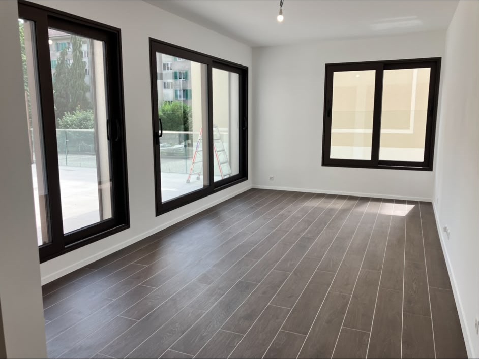 Séjour d’appartement neuf aux murs et plafond peints en blanc, baies vitrées à cadres noirs