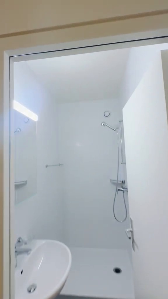 Salle de bains aux murs peints en blanc, douche à l’italienne et lavabo